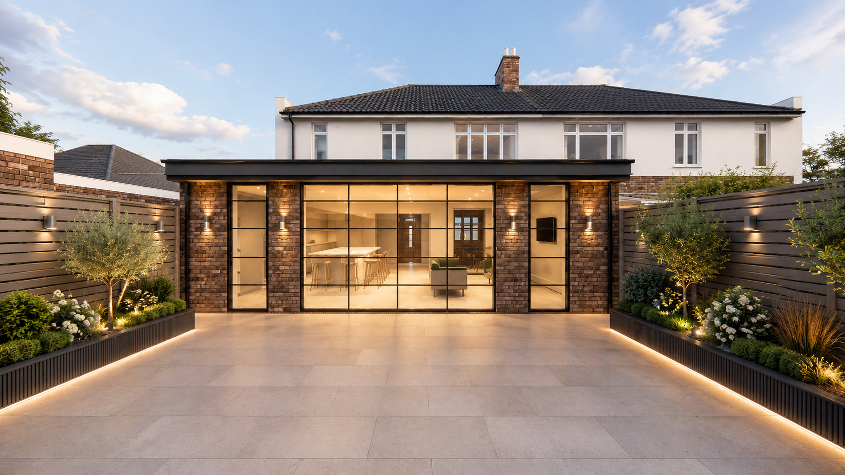 Brick and crittall rear extension lit at dusk with stone patio